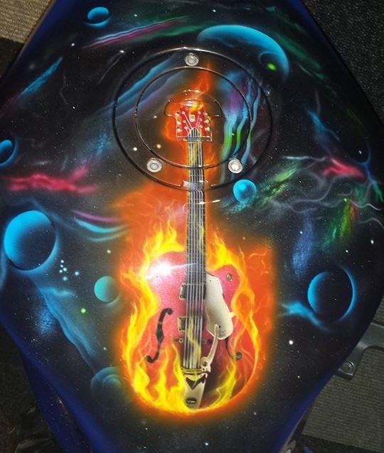 Airbrushed Painting of a Blue Bike with a flaming guitar on a petrol tank with psycodelic space theme background